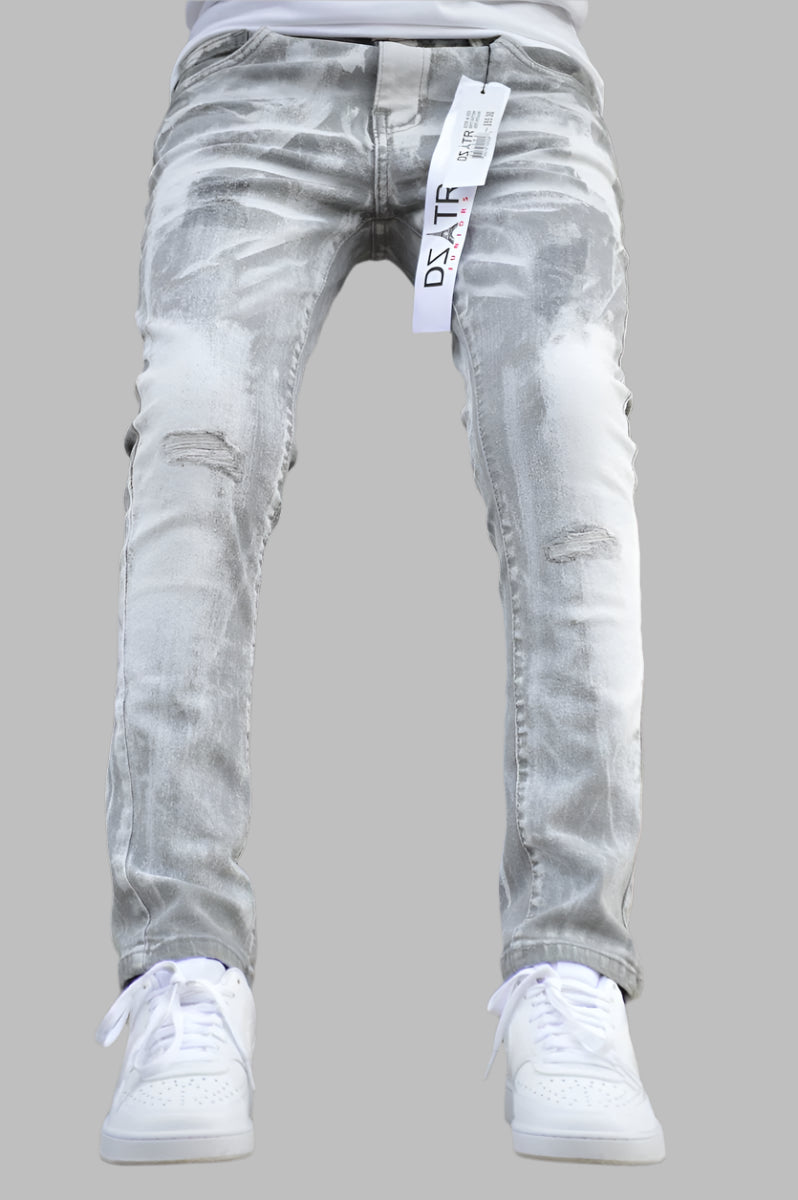 A pair of kids' stretch jeans in Grey Potash color, displayed on a model standing against an industrial background.