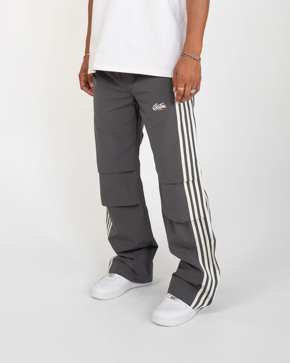The Fogami Pants elevate everyday fashion basics with a relaxed flare silhouette, featuring bold side stripes that fold into front knee pleats for a subtle yet distinctive detail. Crafted from 100% polyester, they include an elastic waistband with an elongated interior drawcord for adjustable comfort. Additional features include side and back pockets and an embroidered logo for a polished streetwear finish.