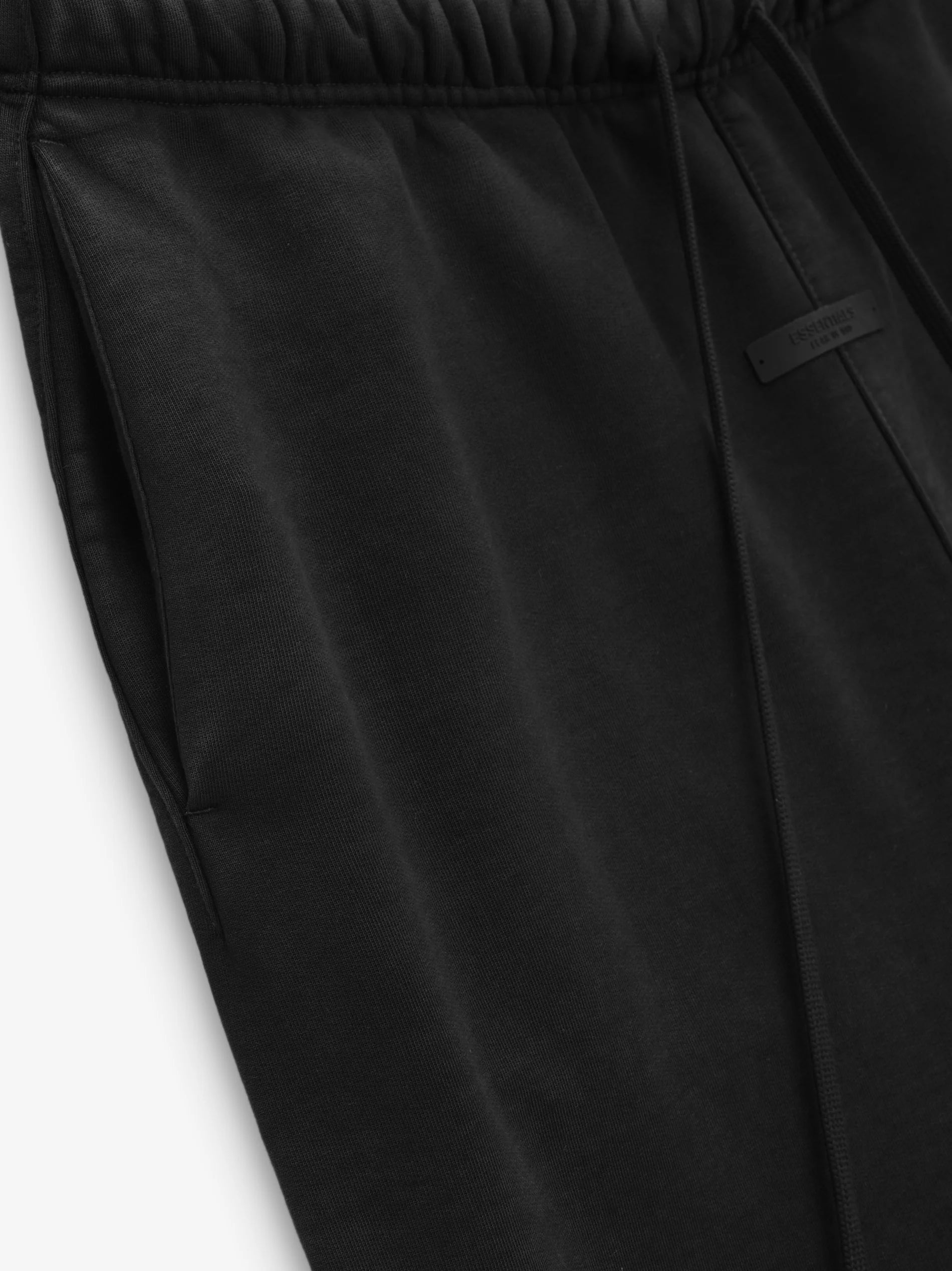 The Heavy Fleece Sweatpant is made from heavyweight 520gsm, 100% cotton fleece in a subtle vintage wash. A collegiate-inspired "Homecoming" graphic is screen-printed on the leg. Additional details include an encased elastic waistband with elongated drawstrings, and side seam pockets. The Essentials Fear of God rubberized label is at the center front.