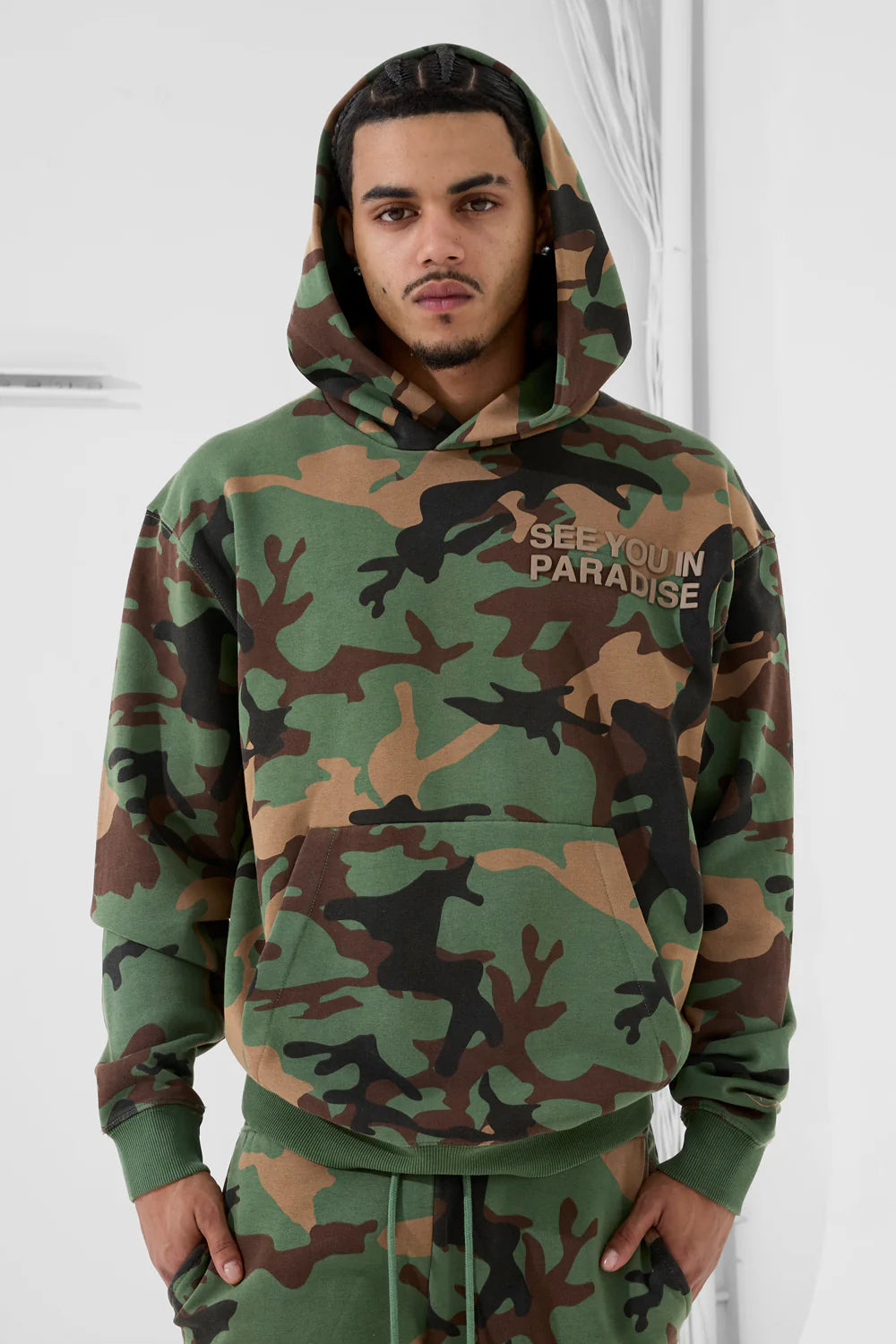 The SYIP Pullover Hoodie in Vintage Camo brings a sharp, technical look with everyday comfort. Designed in a classic hoodie silhouette, it features an all-over camo print and tonal high-density graphics on the chest and back. Made from combed cotton low-shrinkage fleece, this hoodie delivers softness, durability, and a crisp fit. Finished with ribbed cuffs, a ribbed waistband, and a front kangaroo pocket, it pairs perfectly with the matching SYIP Stacked Sweatpants in Vintage Camo.