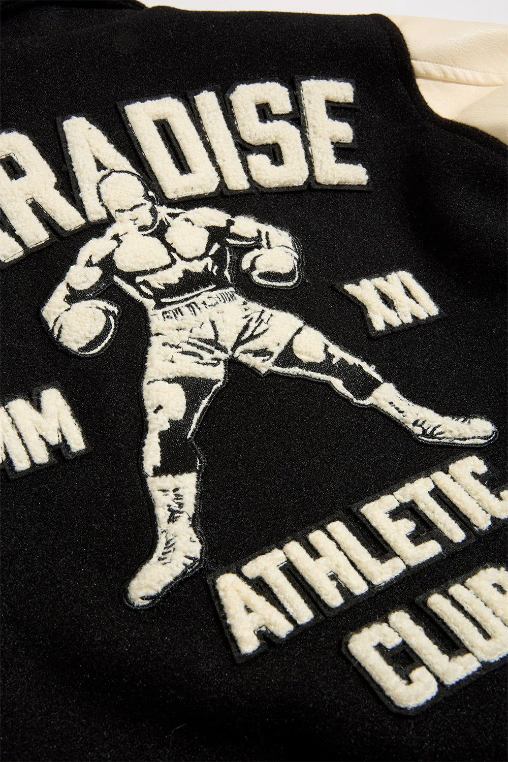 Black Paradise varsity jacket with wool body, vegan leather sleeves, chenille patches, and striped ribbed trims.