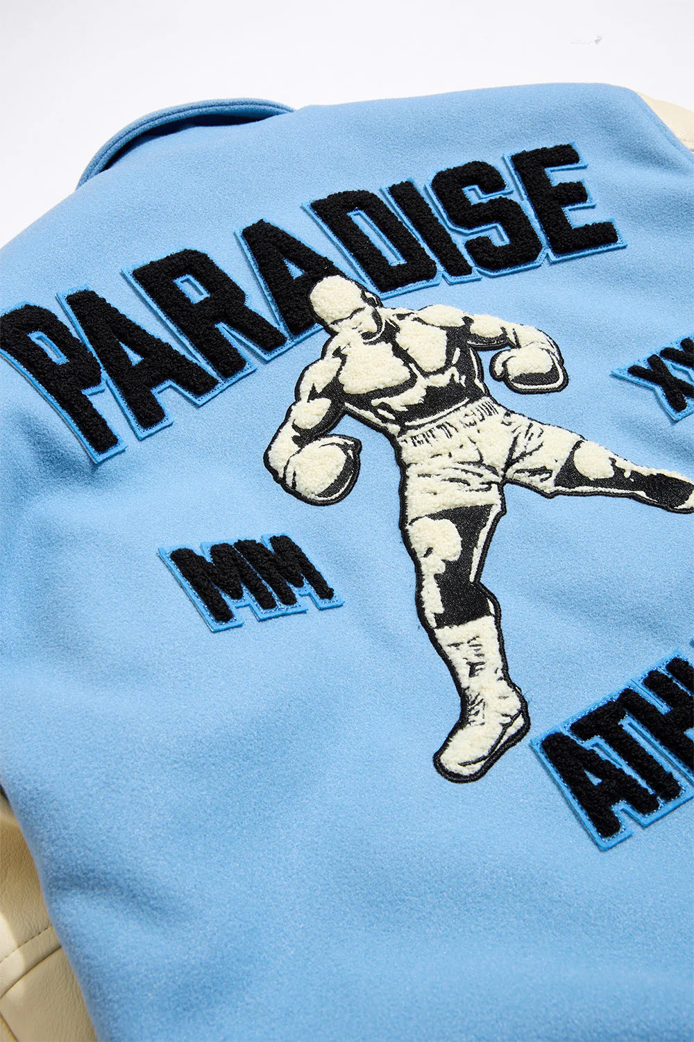 “Paradise Team Varsity Jacket – Sky Blue: wool body, quilted satin lining, vegan leather sleeves, chenille patches, embroidered details, and snap button front.”