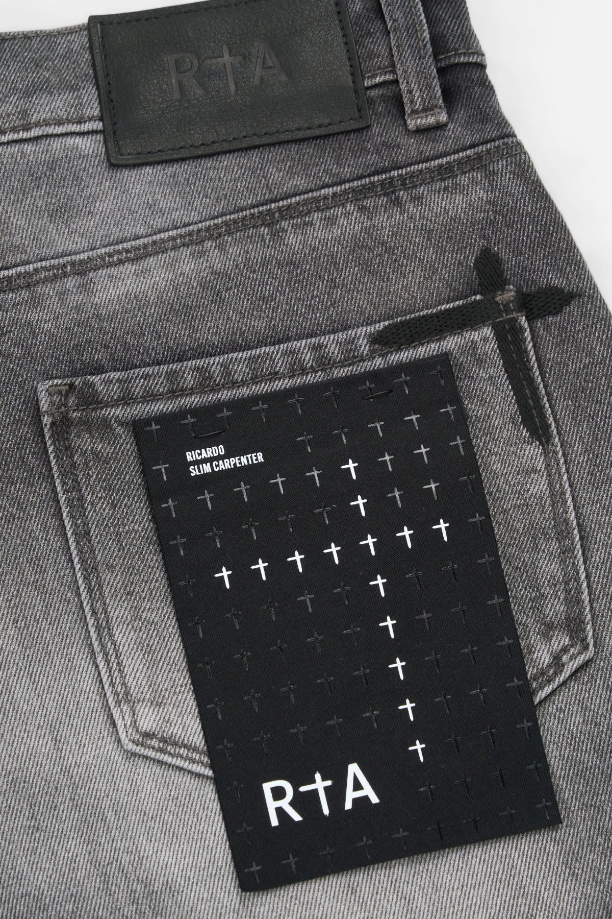 RTA Ricardo Slim Fit Jean in Grey Storm with 3D cross front panels, silver cross emblem, RTA back pocket logo, and leather waistband patch.
