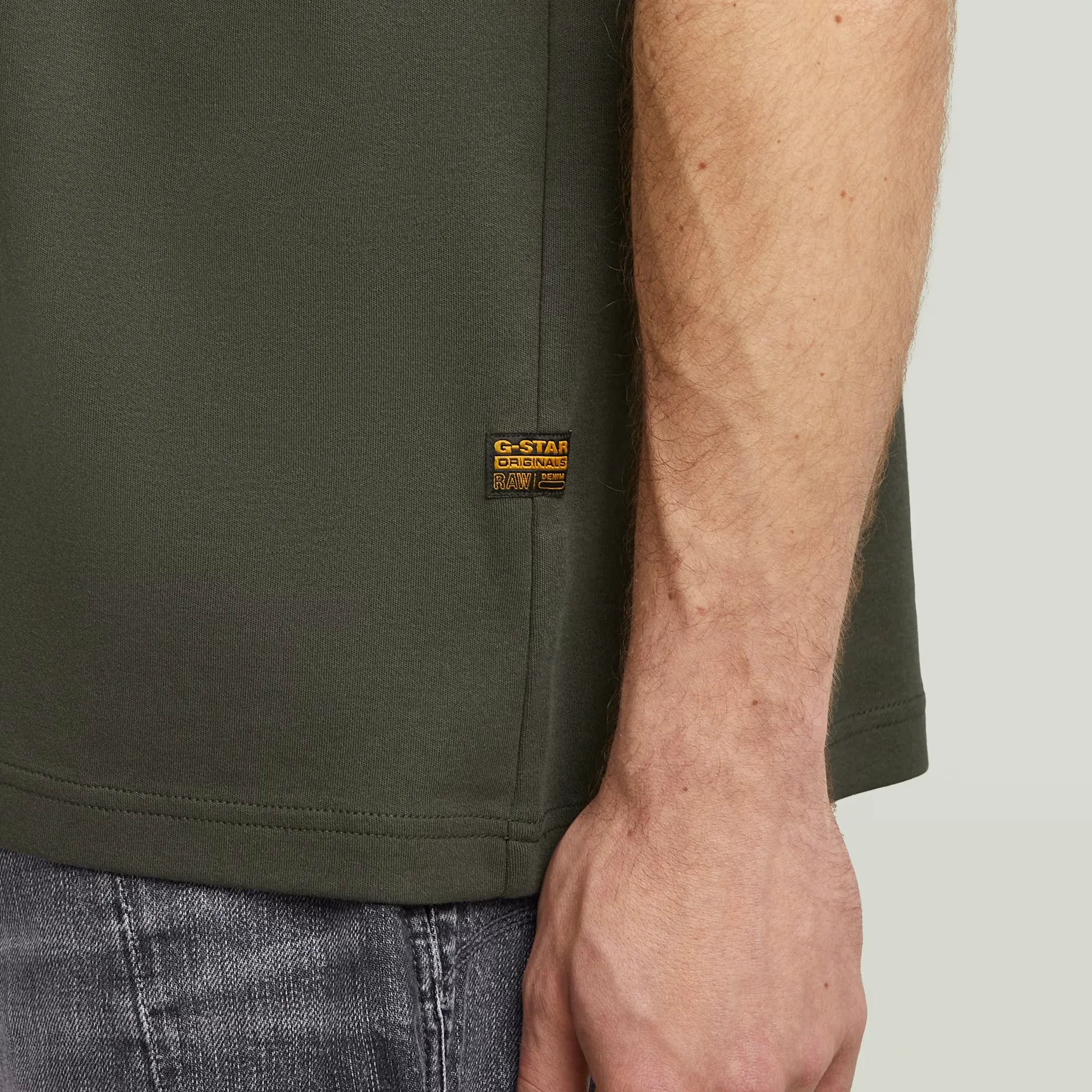 Close-up of a person wearing a green t-shirt with a brand logo on a plain background