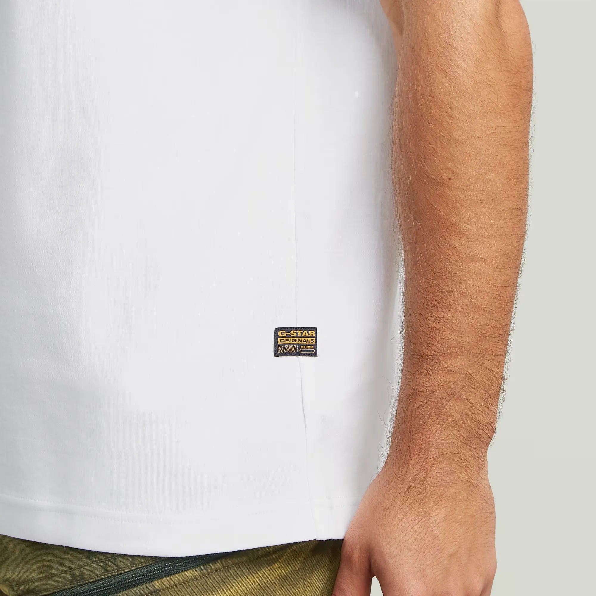 Close-up of a person wearing a white t-shirt with a brand label on a plain background