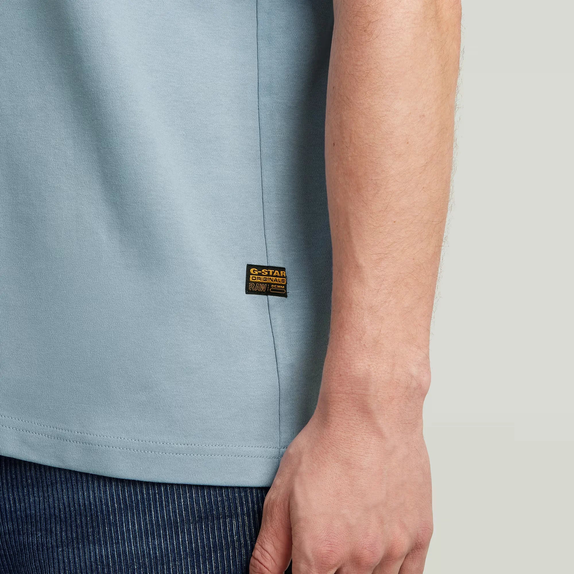 Light blue t-shirt with a brand label on a neutral background