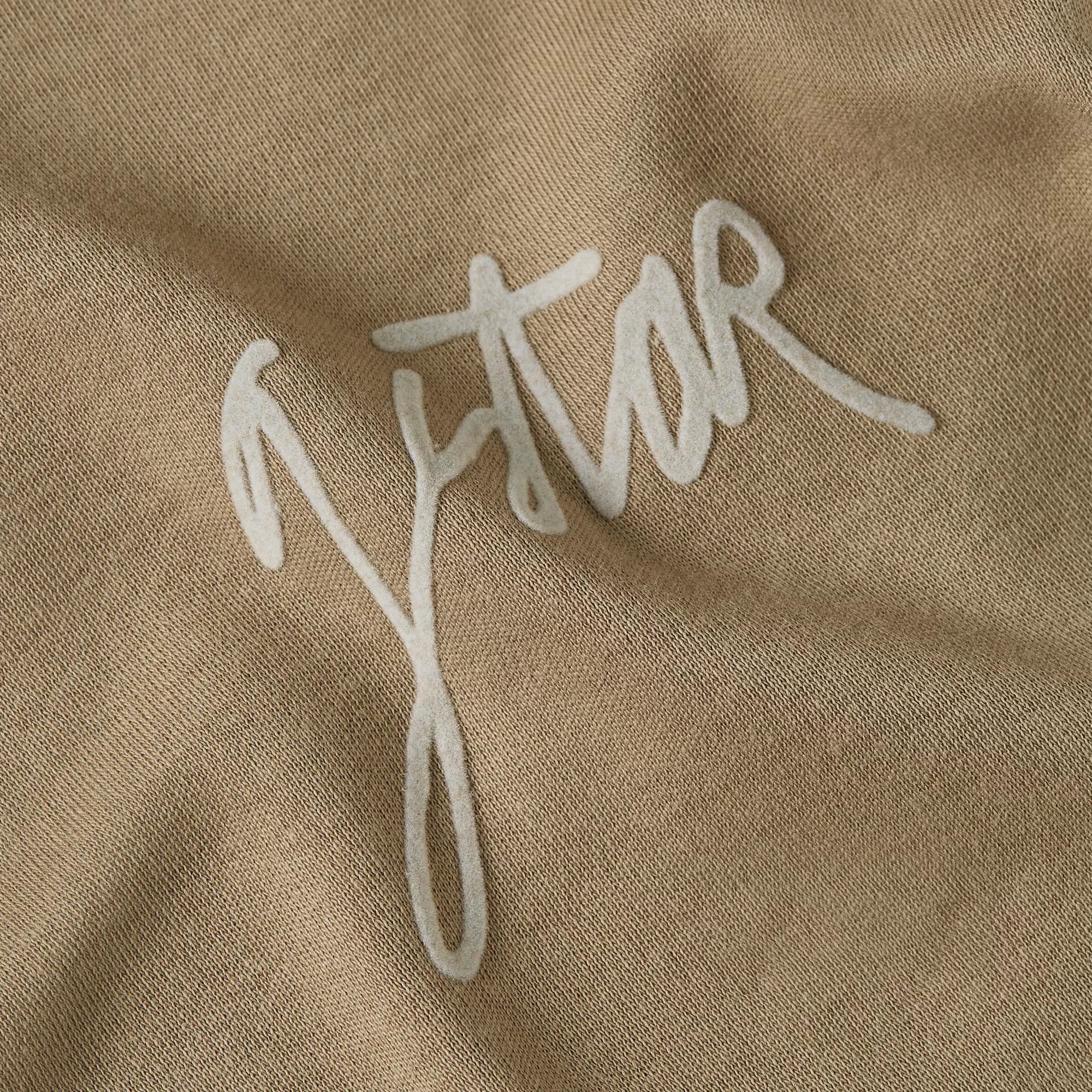 Close-up of a beige fabric with 'Jestar' embroidered in white thread.