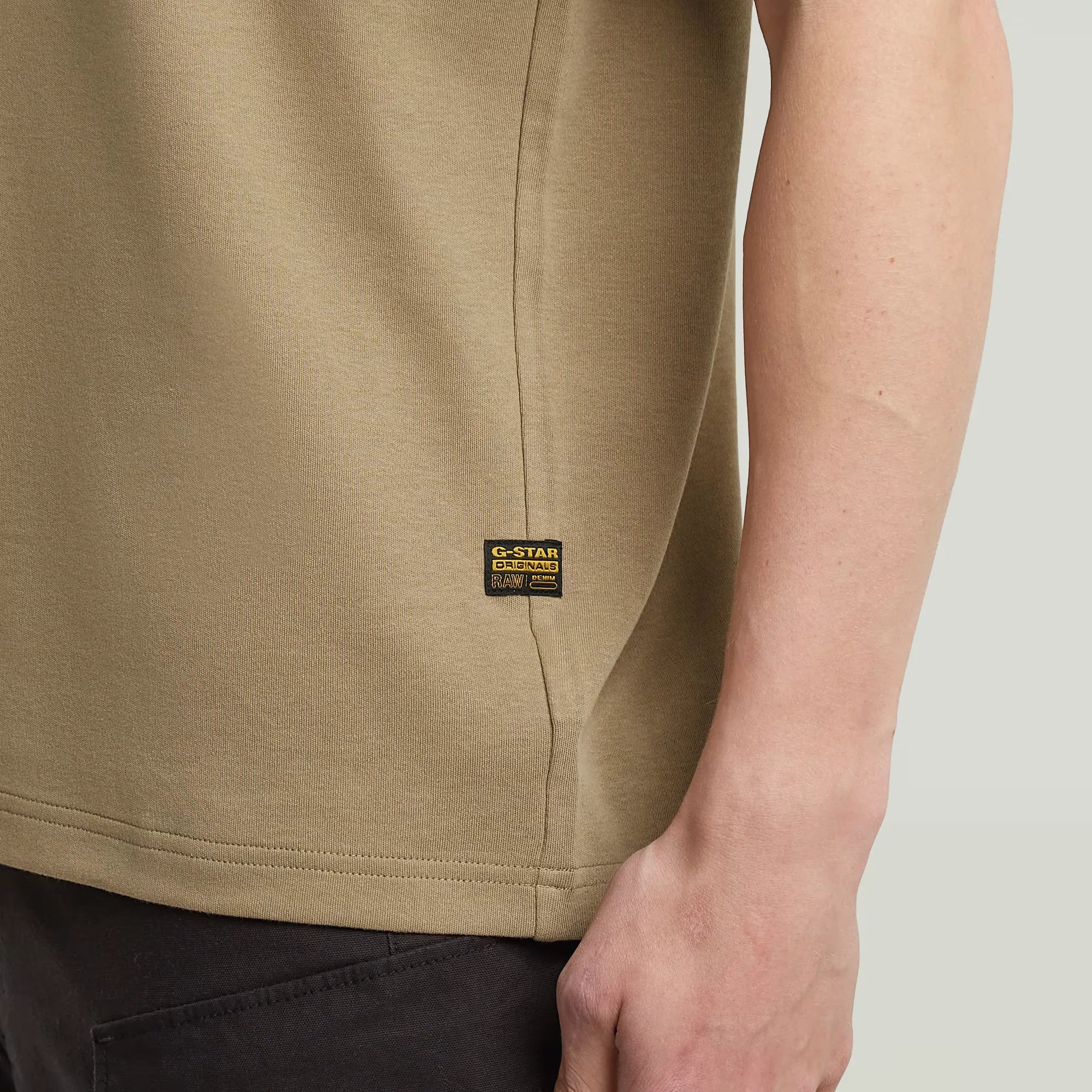 Close-up of a beige G-Star Raw t-shirt with a visible brand label on a neutral background.