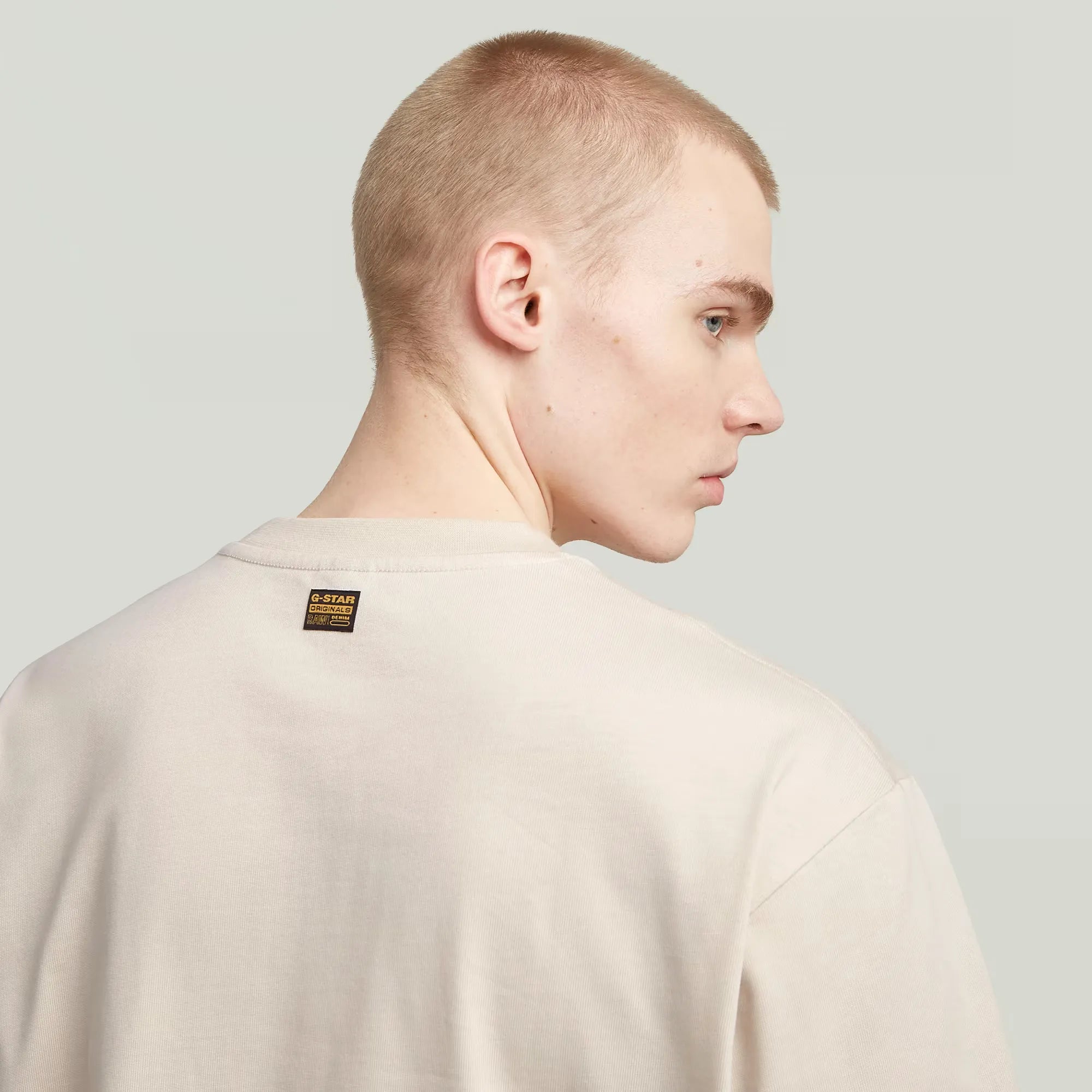 Person wearing a beige sweater with a brand label on a light gray background