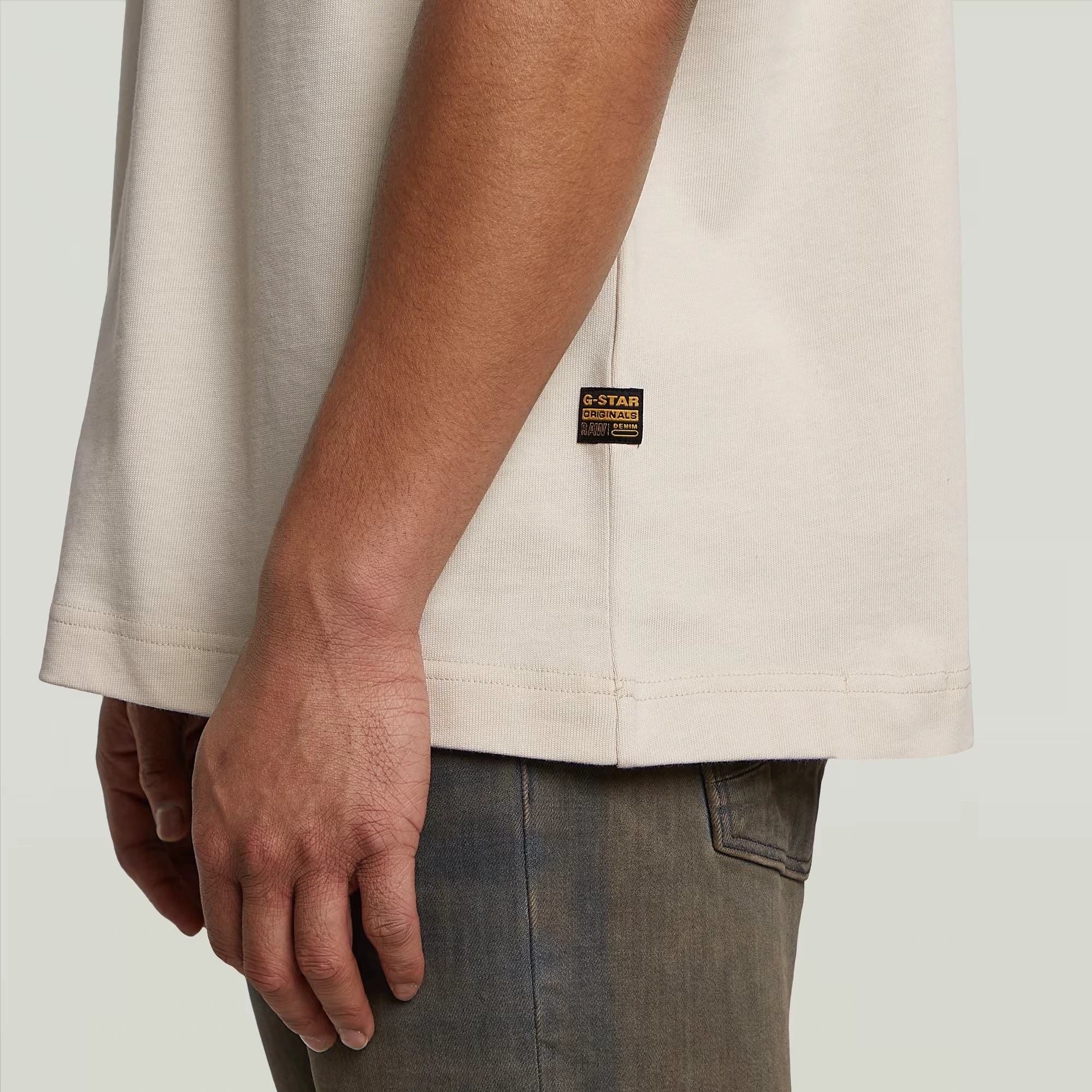 Close-up of a person wearing a beige jacket with a brand label on a light gray background