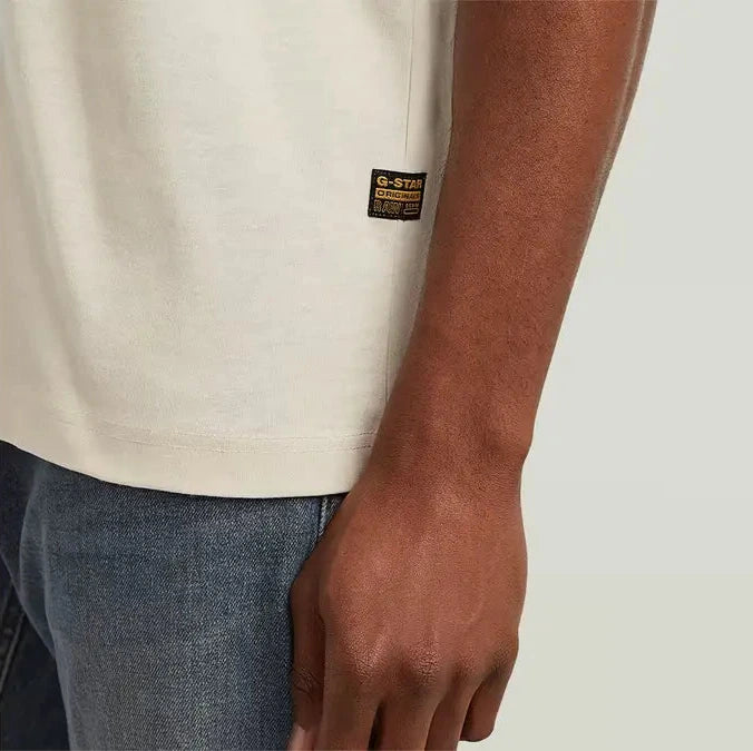 Person wearing a beige t-shirt with a brand logo on a plain background