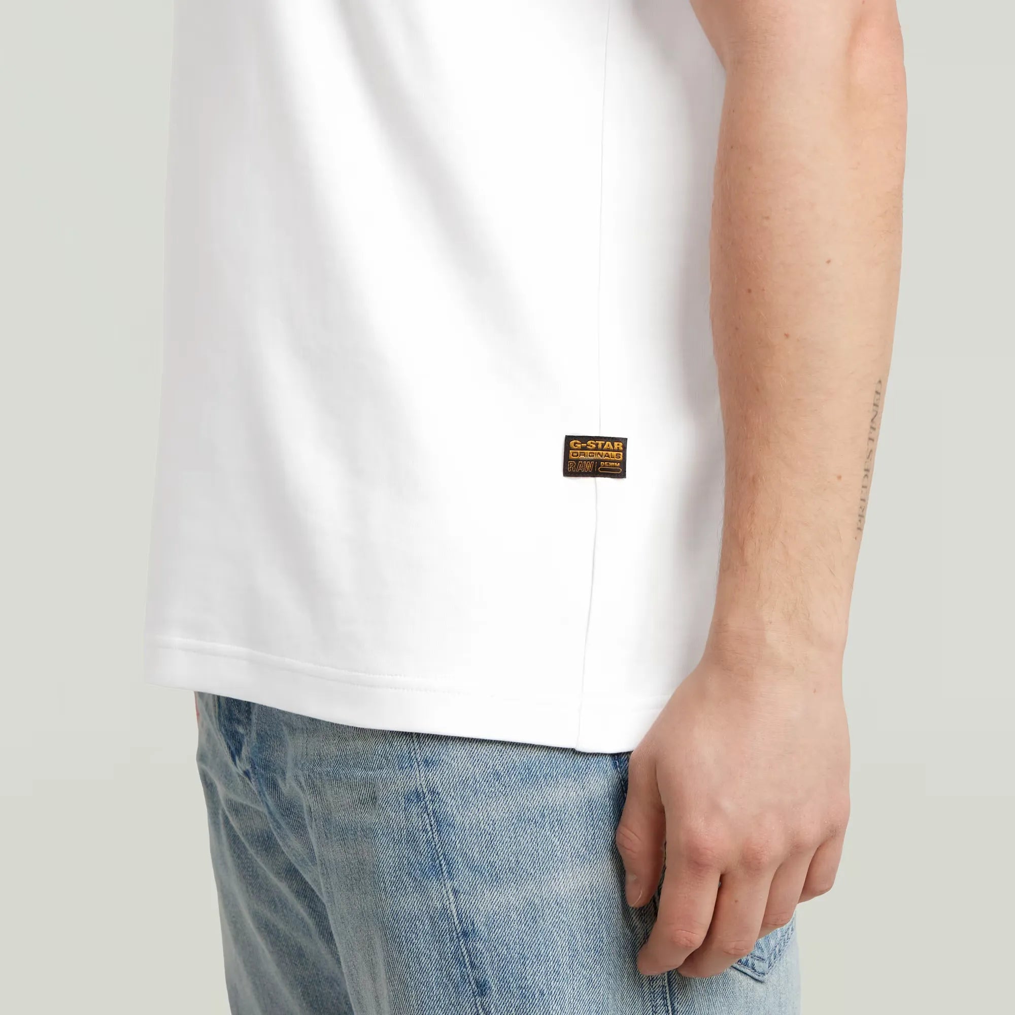 Person wearing a white t-shirt with a brand logo and blue jeans on a light gray background