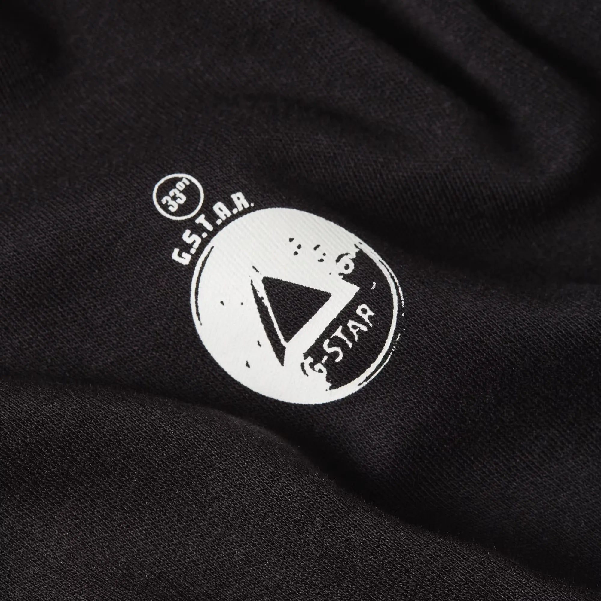 Close-up of a black fabric with a white logo featuring 'G.S.T.A.R.' text and design.