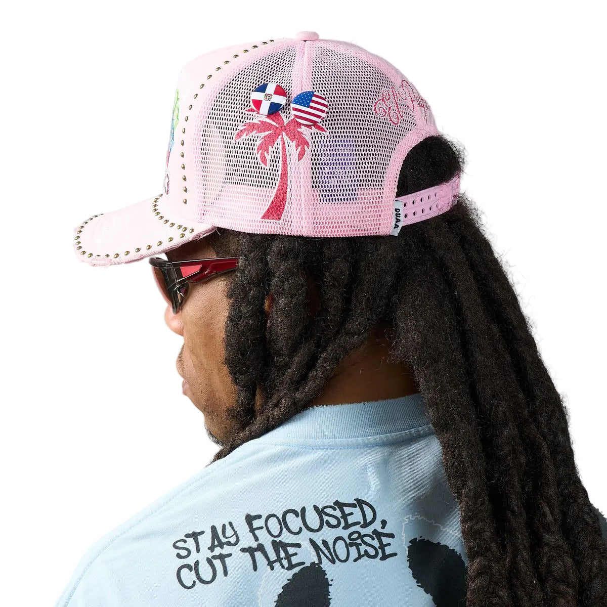 DUAA Air Hat featuring pink front panel, mesh back, multicolor graffiti embroidery, bee and 33 patch details, gold stud trim, and distressed brim snapback design.