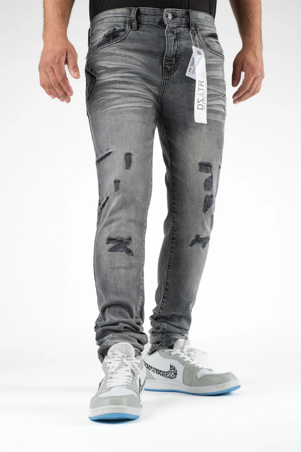 Person wearing gray distressed jeans with a brand tag on a white background