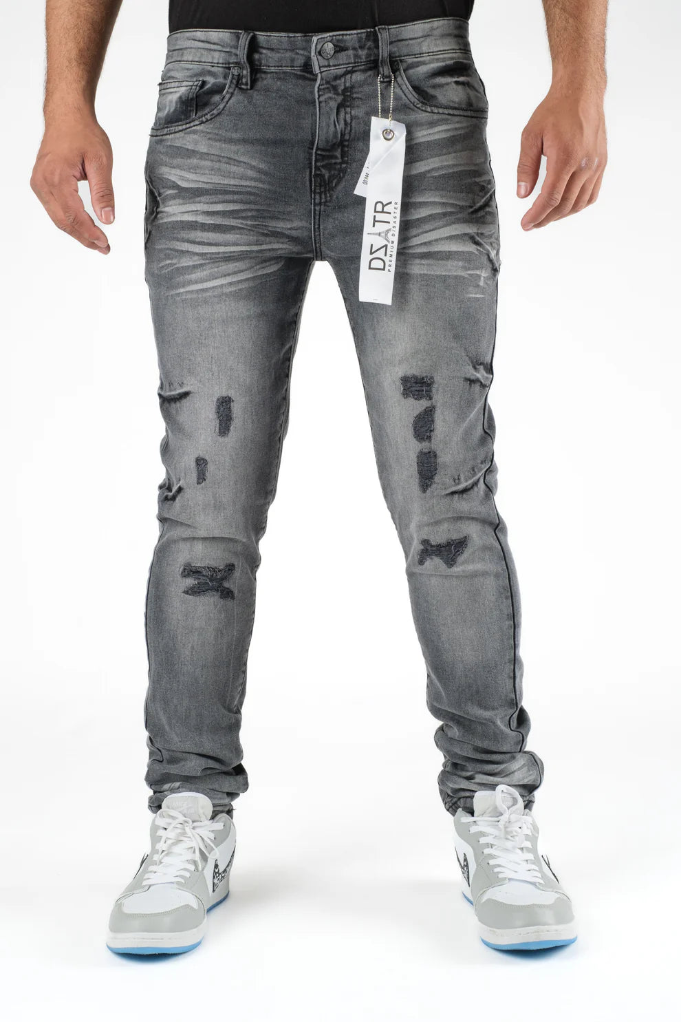 Person wearing gray distressed jeans with a brand tag on a white background