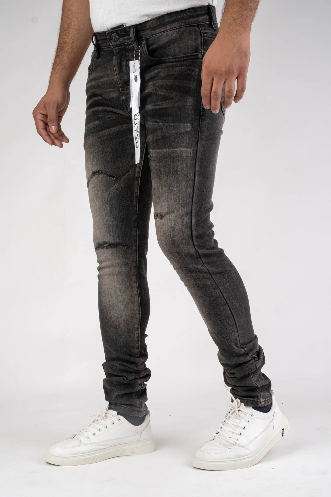 Person wearing black distressed jeans with a white brand label on a white background