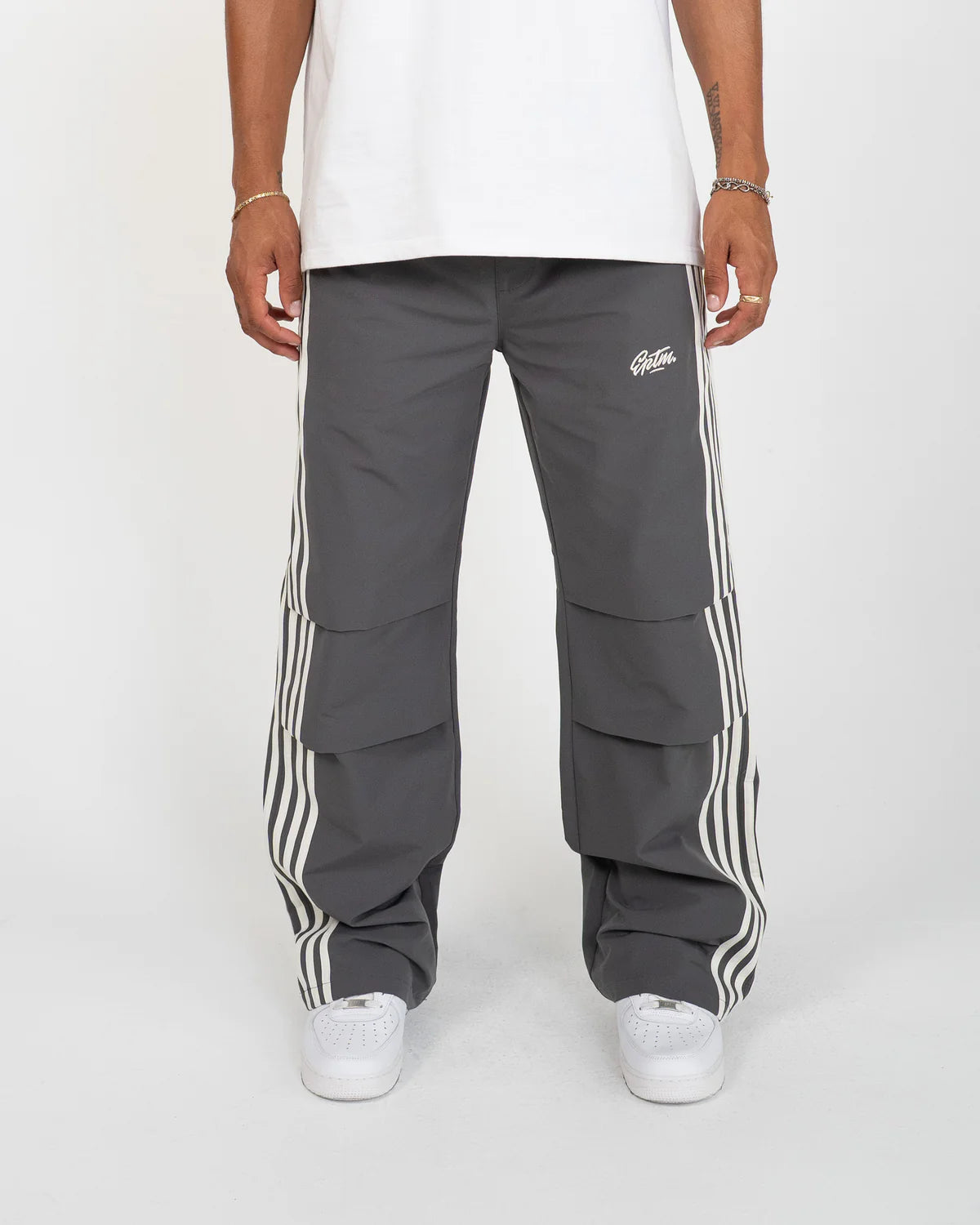 The Fogami Pants elevate everyday fashion basics with a relaxed flare silhouette, featuring bold side stripes that fold into front knee pleats for a subtle yet distinctive detail. Crafted from 100% polyester, they include an elastic waistband with an elongated interior drawcord for adjustable comfort. Additional features include side and back pockets and an embroidered logo for a polished streetwear finish.