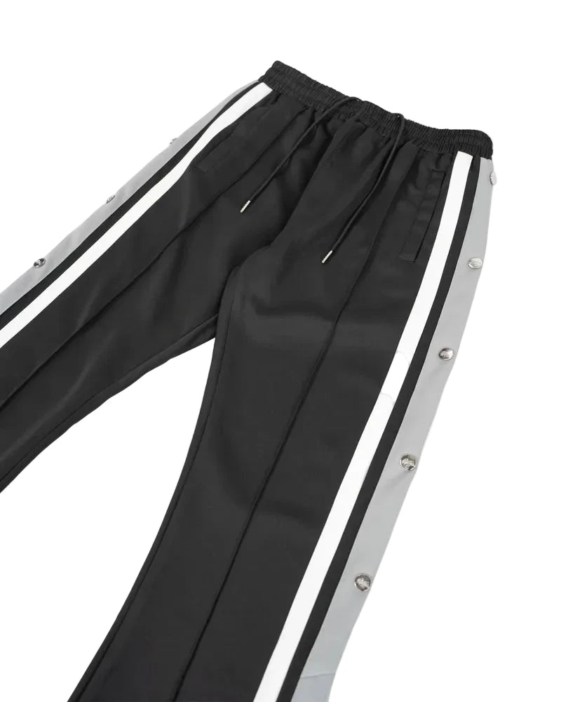 EPTM Gully Track Pants in black with side seam stripes, metal logo snap buttons, front pintucks, and relaxed flare fit