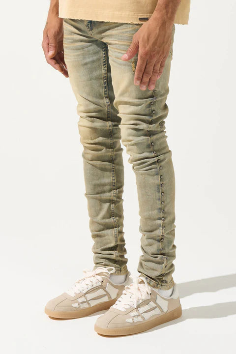 SERENEDE® EXO vintage earth brown jeans with raw sienna overdyed wash, fitted construction, metal studs along stitching, whiskering and fading, leather waistband patch, holographic hangtag, and branded hardware