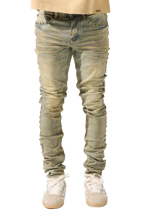 SERENEDE® EXO vintage earth brown jeans with raw sienna overdyed wash, fitted construction, metal studs along stitching, whiskering and fading, leather waistband patch, holographic hangtag, and branded hardware