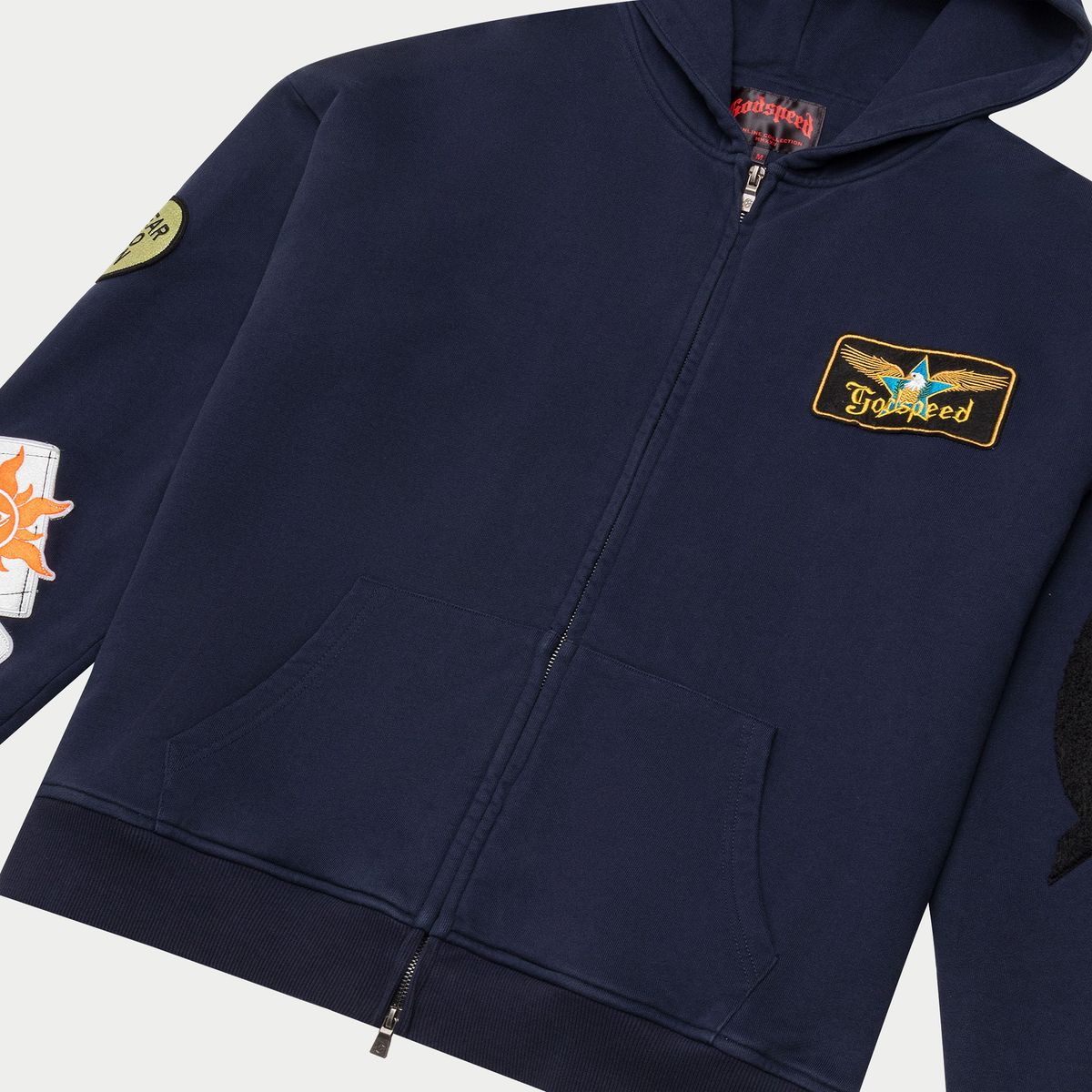 The GS Squadron Hoodie in Navy delivers a clean mix of comfort and utility. Made from medium-weight 100% cotton, it offers a soft, breathable feel ideal for everyday wear. Distinctive patch details on the sleeve and hood give it a signature Godspeed look, adding character without sacrificing simplicity. Finished with a full zip front and a relaxed fit, this hoodie brings effortless style to any rotation.