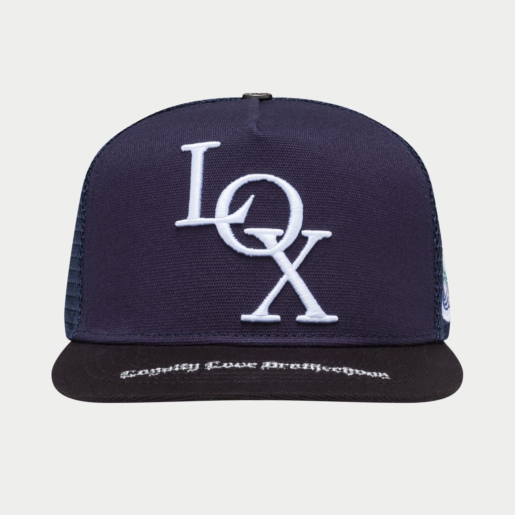 Black and navy Legacy Trucker hat with mesh back and snapback closure, inspired by Living Off Xperience album, packaged in limited-edition commemorative box.