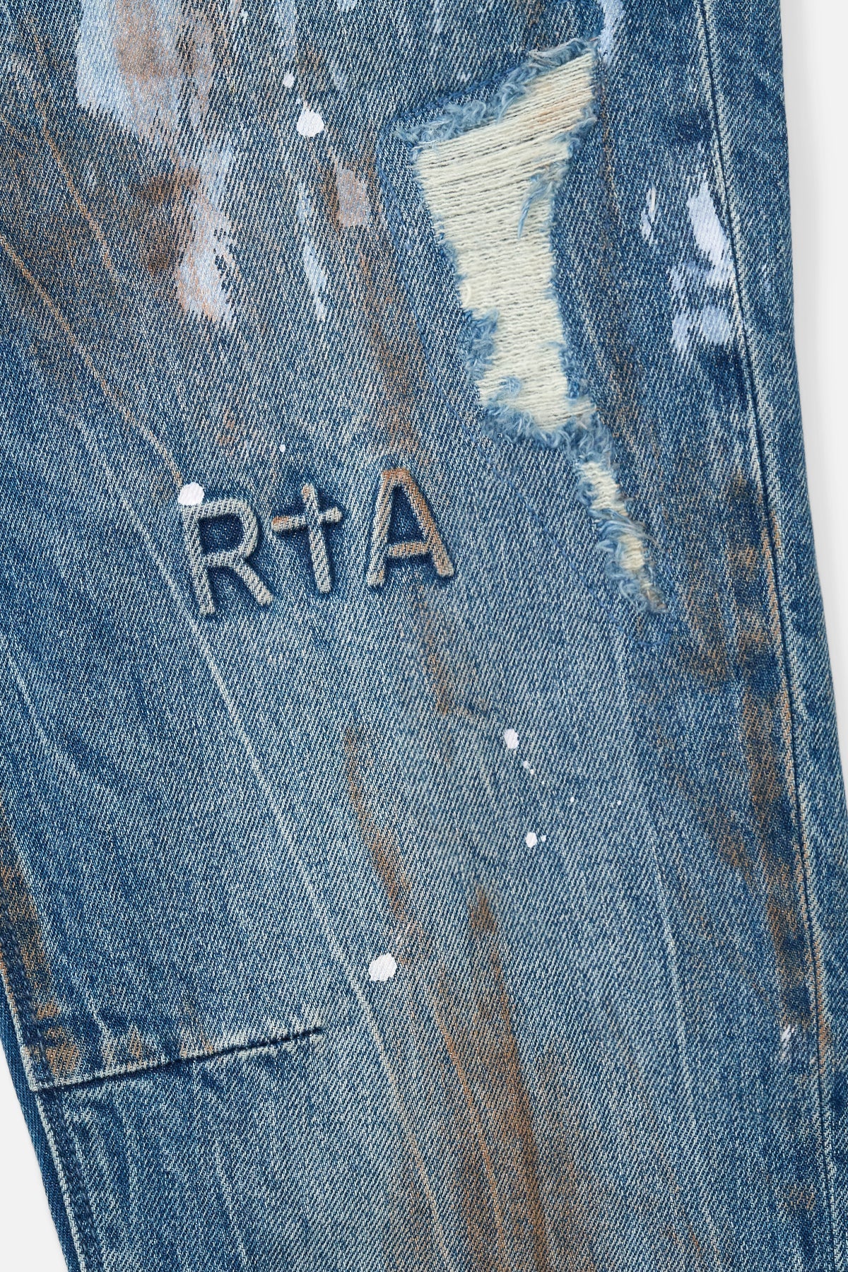 RTA Clayton Skinny Jean in Glitch Blue with distressed finish, paint splatter, embossed logo, and dagger seams.