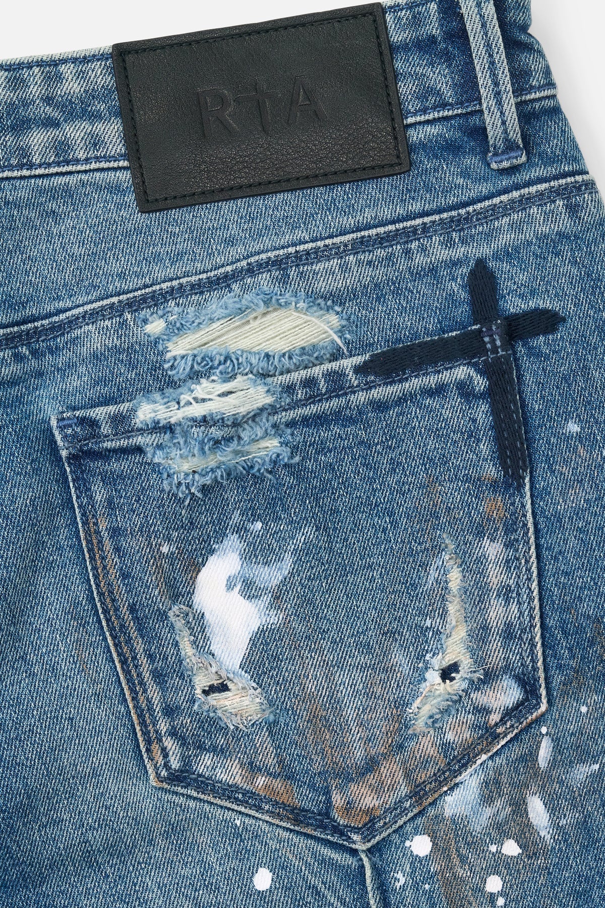 RTA Clayton Skinny Jean in Glitch Blue with distressed finish, paint splatter, embossed logo, and dagger seams.