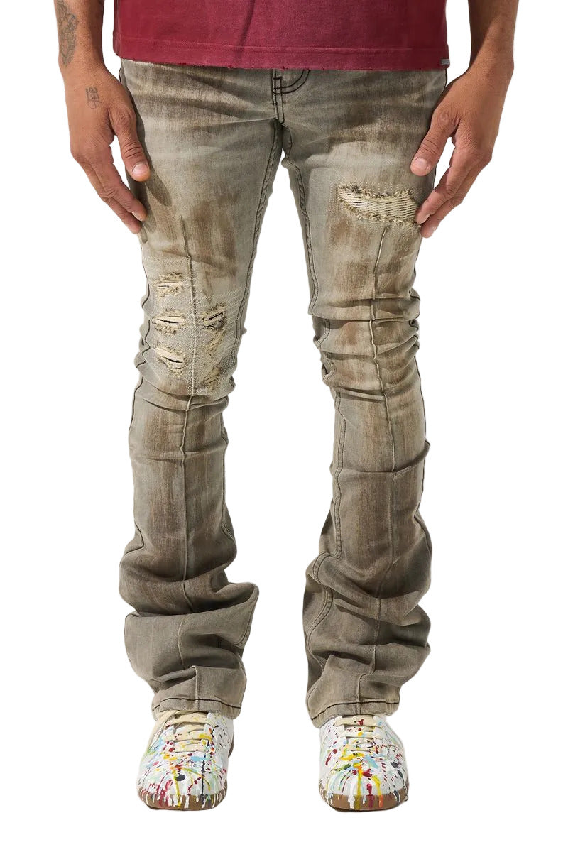 SERENEDE® Nanodust stacked jeans in vintage grey-taupe denim with heavy knee distressing, rust-brown overspray, and extended stacked inseam.