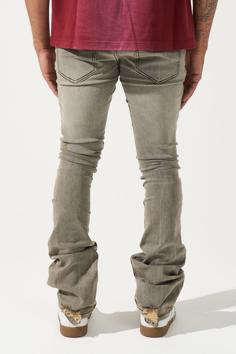 SERENEDE® Nanodust stacked jeans in vintage grey-taupe denim with heavy knee distressing, rust-brown overspray, and extended stacked inseam.