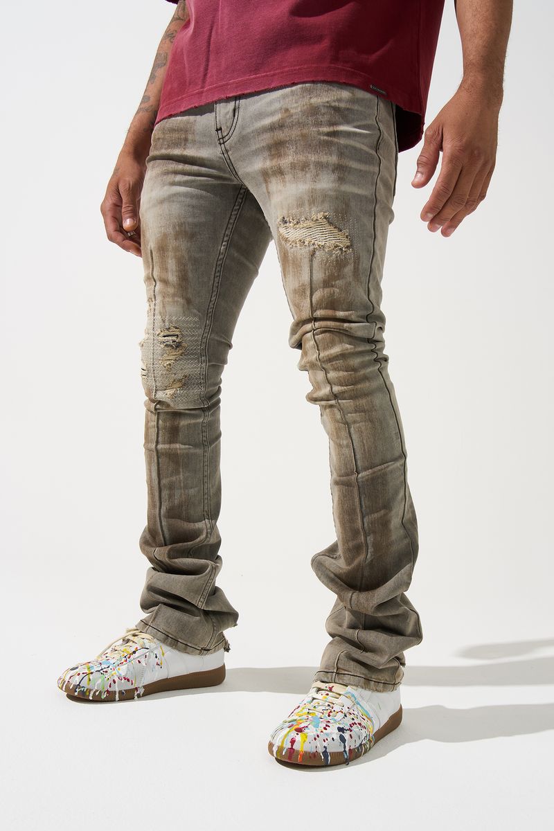 SERENEDE® Nanodust stacked jeans in vintage grey-taupe denim with heavy knee distressing, rust-brown overspray, and extended stacked inseam.
