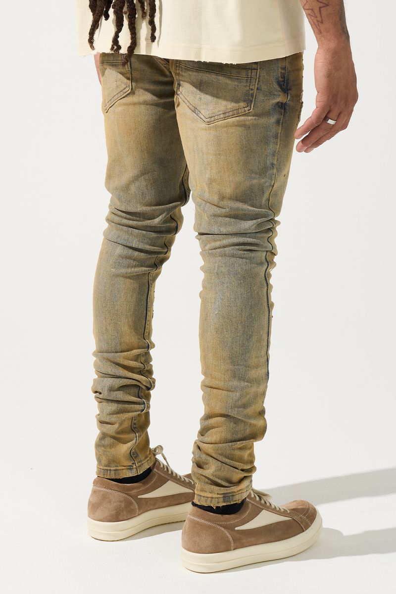 SERENEDE® Networth fitted stacked jeans in sand-washed denim with hot-fix crystal detailing, fading, and raw hem finish.