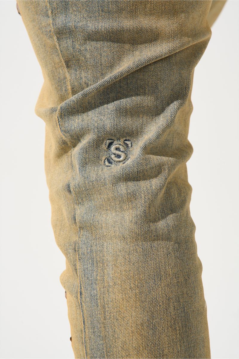 SERENEDE® Networth fitted stacked jeans in sand-washed denim with hot-fix crystal detailing, fading, and raw hem finish.