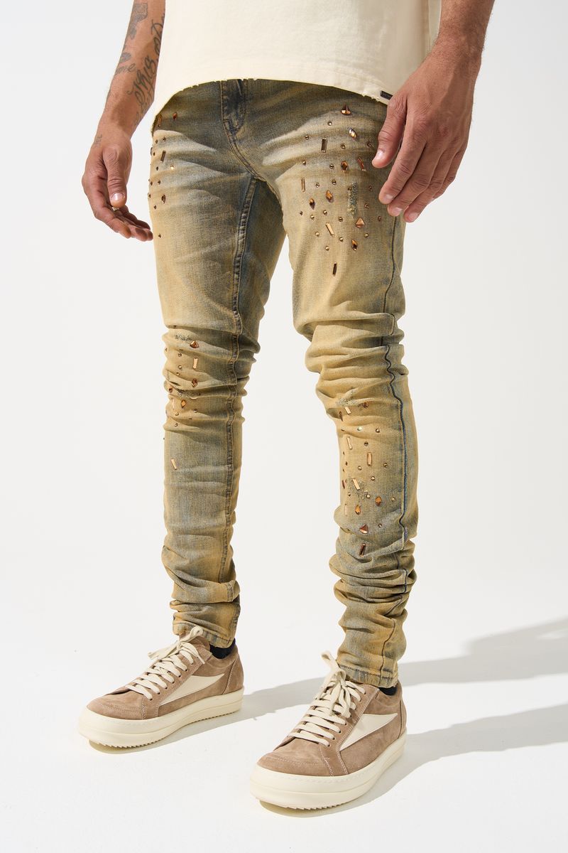 SERENEDE® Networth fitted stacked jeans in sand-washed denim with hot-fix crystal detailing, fading, and raw hem finish.