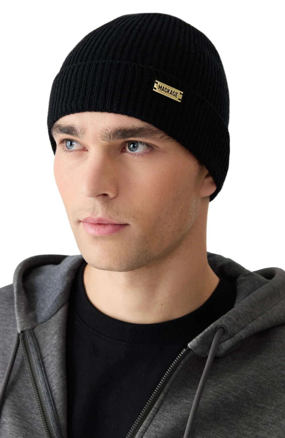 Man wearing a black beanie with a brand logo on a light gray background