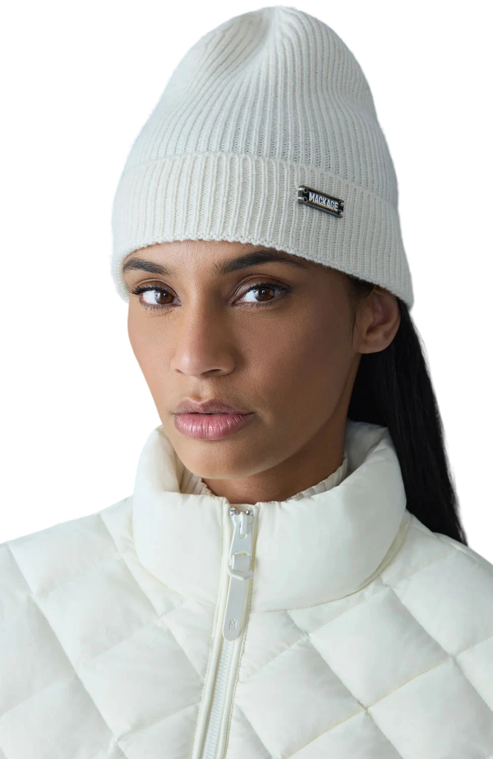 Person wearing a white knit beanie with a brand logo against a gray background