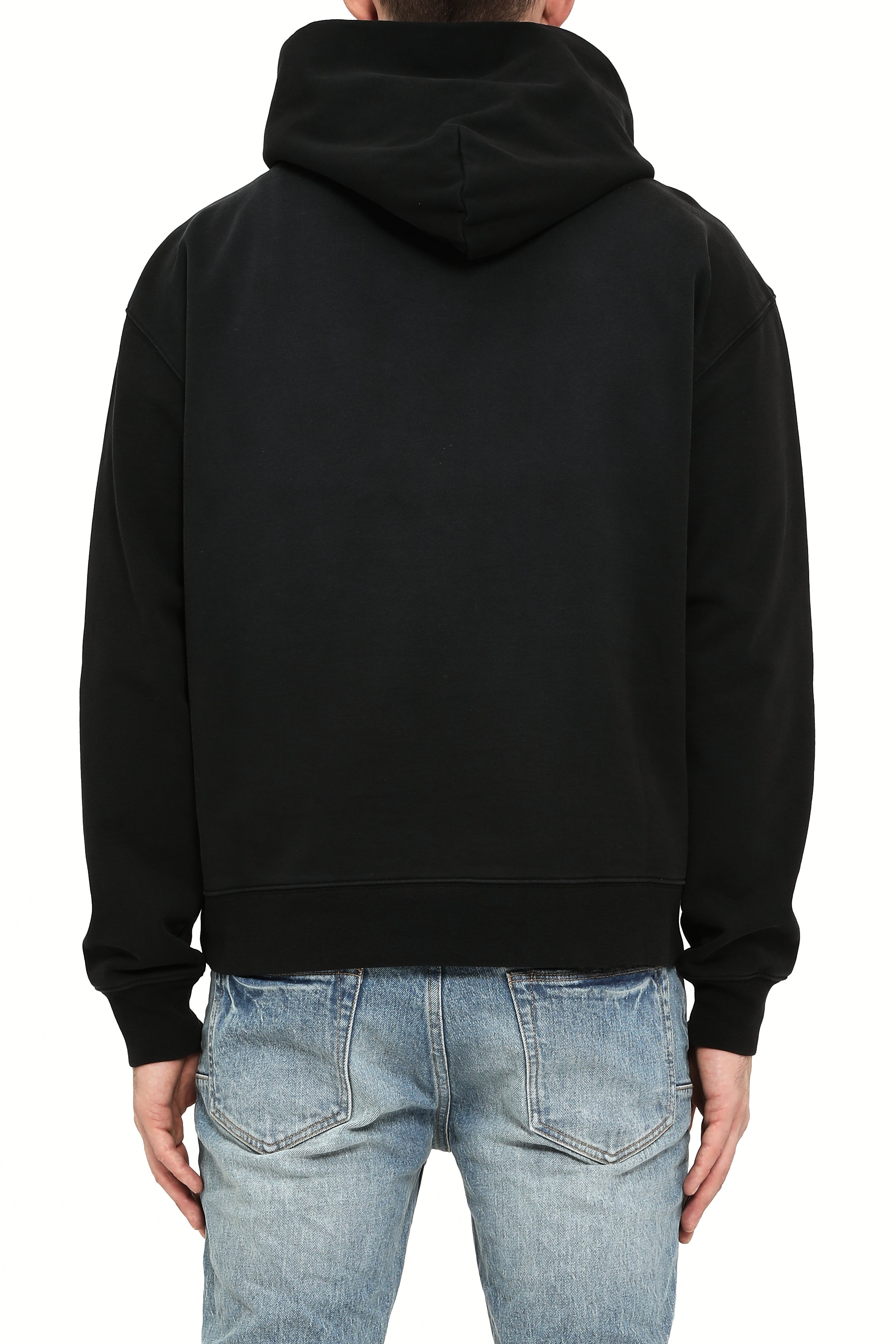 Person wearing a black hoodie and light blue jeans on a white background