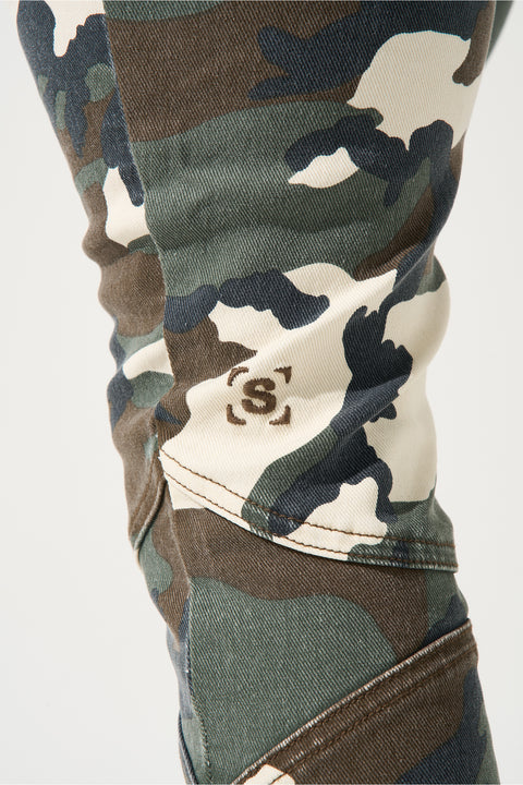SERENEDE® SYNC Jeans in desert moss camo with fitted construction, biker panel details, embroidered [S]® logo, and holographic hangtag.
