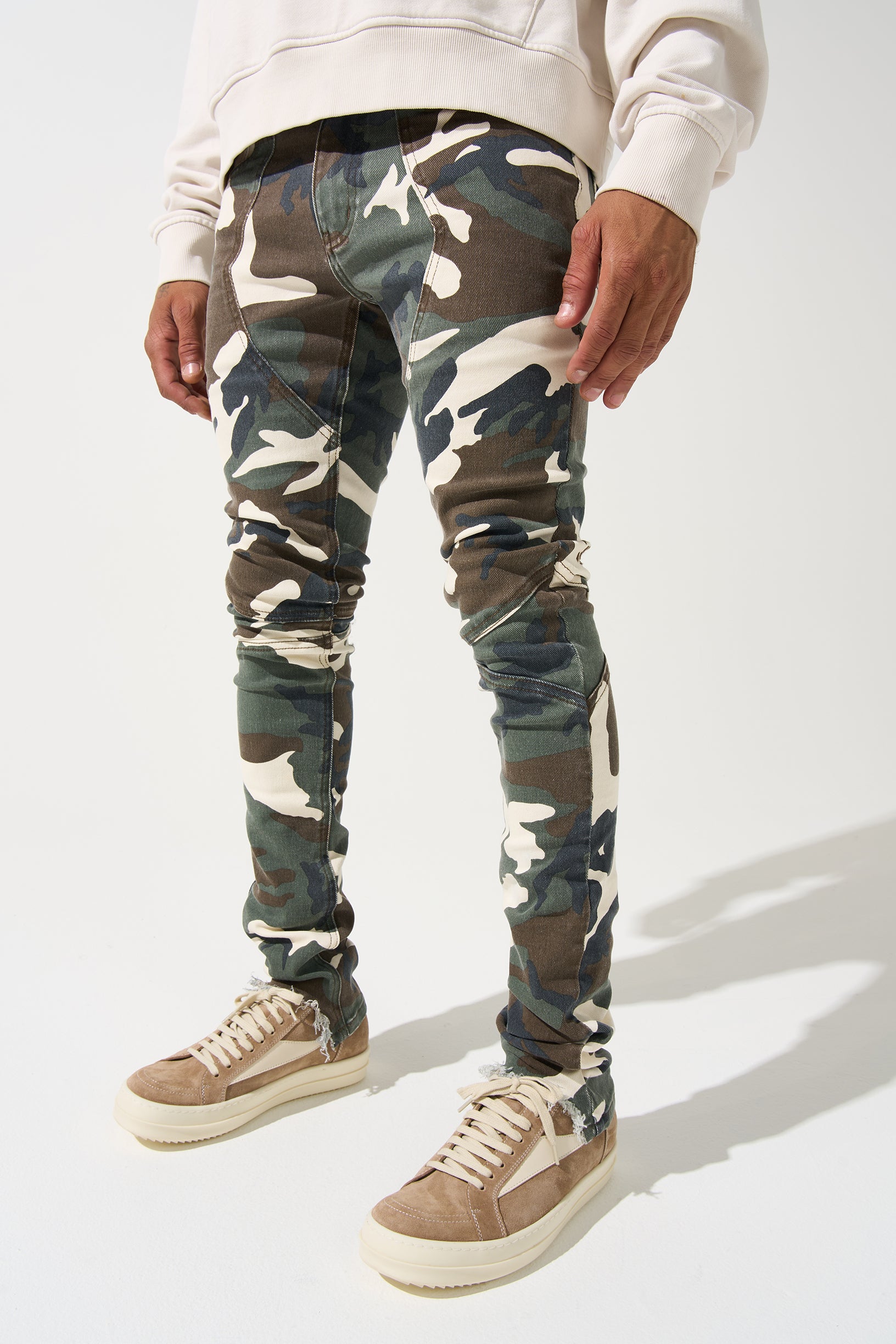 SERENEDE® SYNC Jeans in desert moss camo with fitted construction, biker panel details, embroidered [S]® logo, and holographic hangtag.